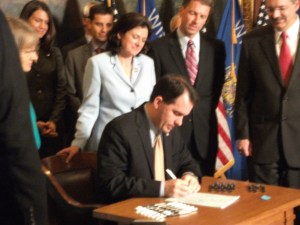 Governor Scott Walker signs Voter ID bill as Republican legislators look on.