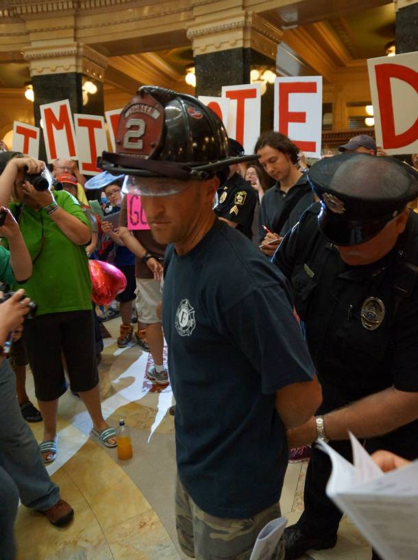 Firefighter Ted Higgins being handcuffed by Cap Police. Photo by Leslie Peterson
